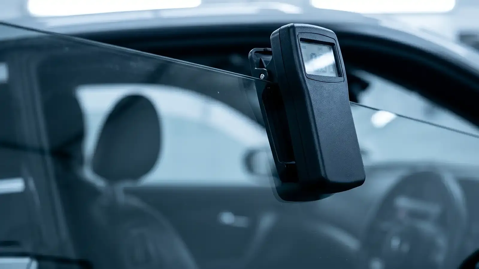 Handheld digital VLT meter clipped onto a tinted car window measuring visible light transmission during a New York state inspection.